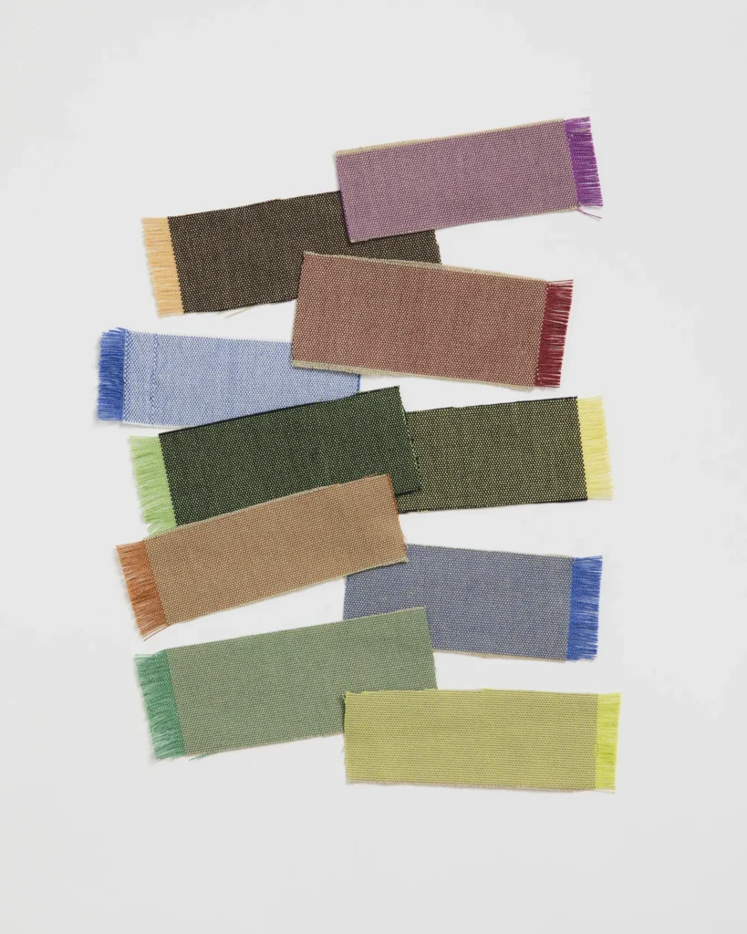 Colourful textile samples in different weaves and textures, arranged in a layered composition against a light background.